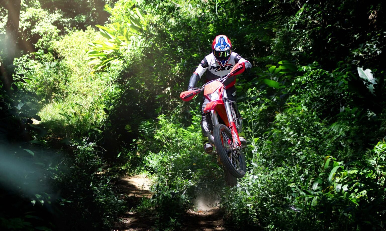 Piloto com roupa branca e vermelha saltando com a MXF 300 TSX em uma pista de terra.