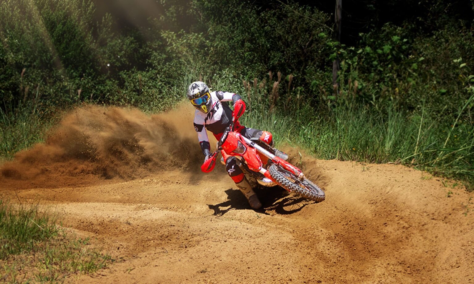 Piloto acelerando forte a MXF 250 TSX em curva de terra, levantando uma grande nuvem de poeira e detritos.