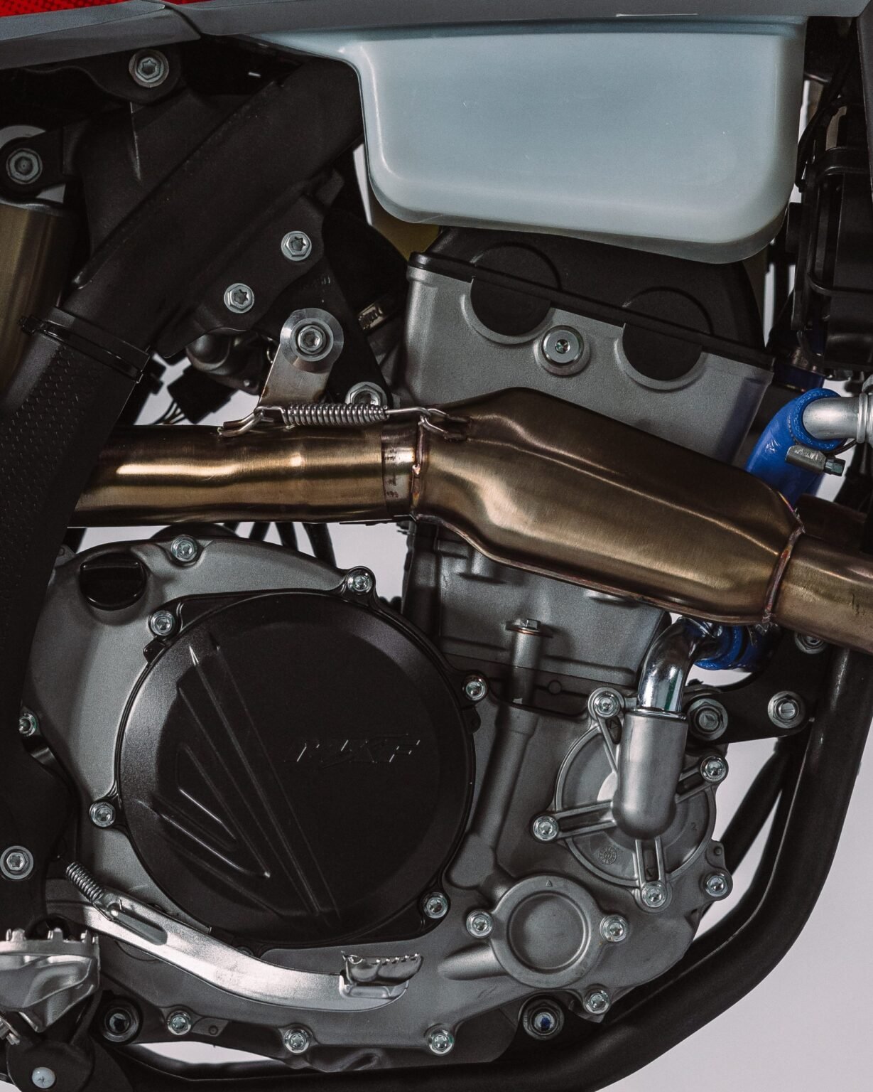 Detalhe do motor da MXF 250 RXi mostrando a tampa do magneto, o escapamento e o tanque de expansão.