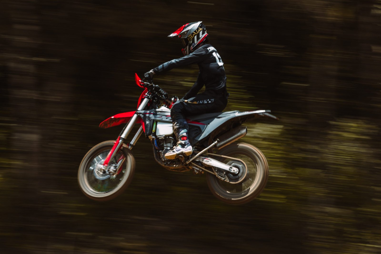 Piloto saltando lateralmente com a MXF 250 RXi (Piloto em preto e branco) em alta velocidade contra fundo escuro.