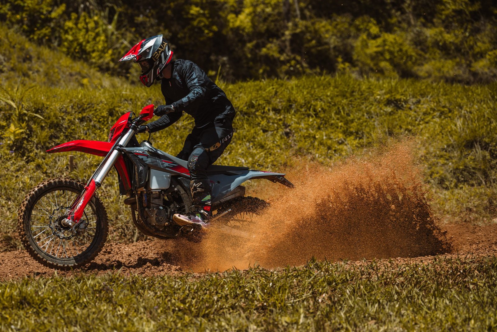 Piloto saindo de curva na MXF 250 RXi, levantando terra e cascalho no ar.
