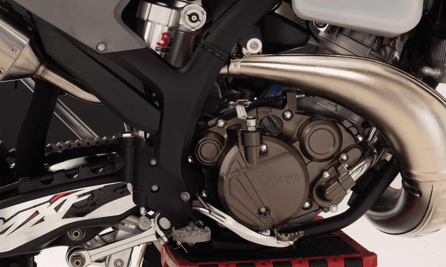 Motor 2 tempos da MXF 250 TSX com escapamento de câmara de expansão cromada, pedal de câmbio e logo MXF na tampa.