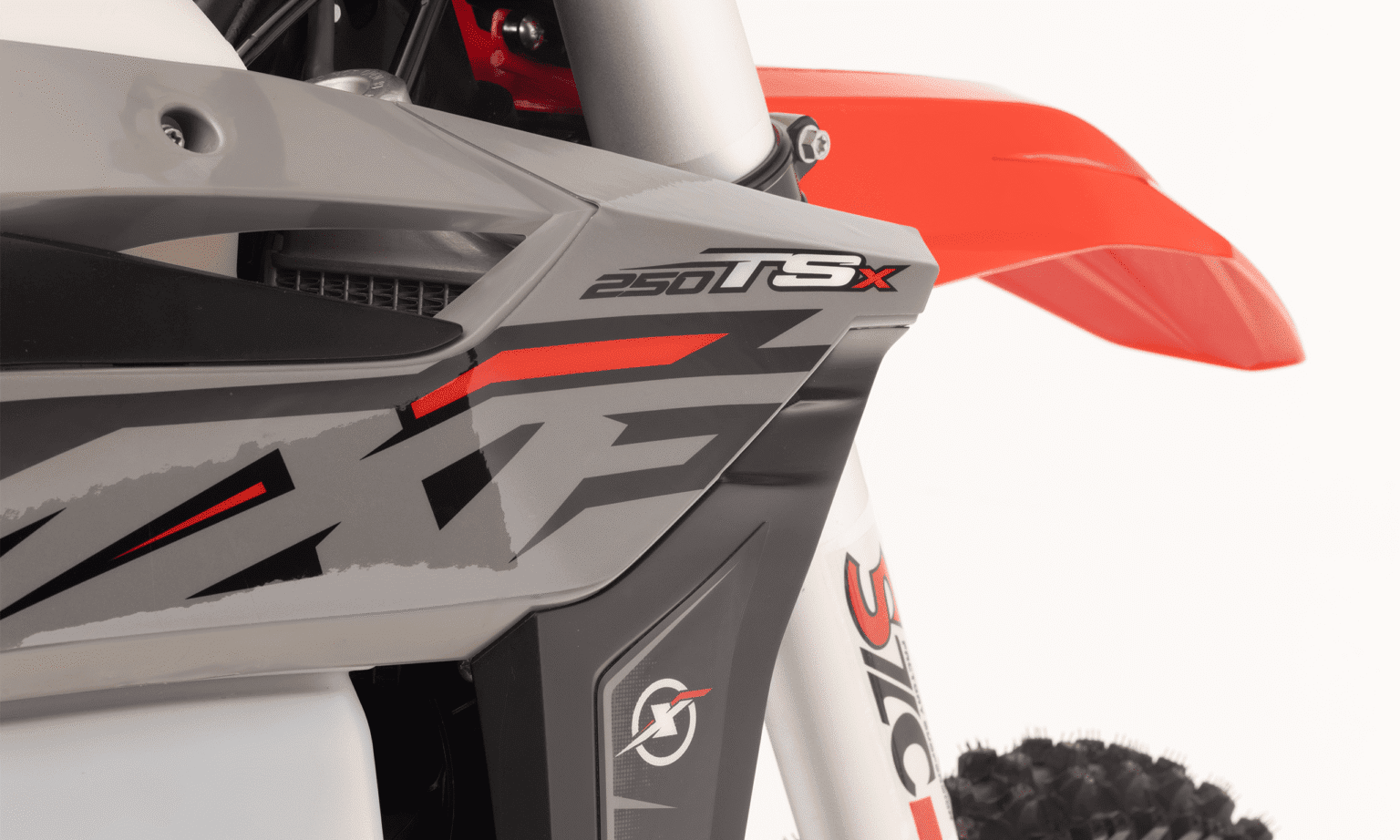 Close no grafismo "250 TSX" na carenagem lateral cinza e vermelha, e a base da suspensão dianteira.