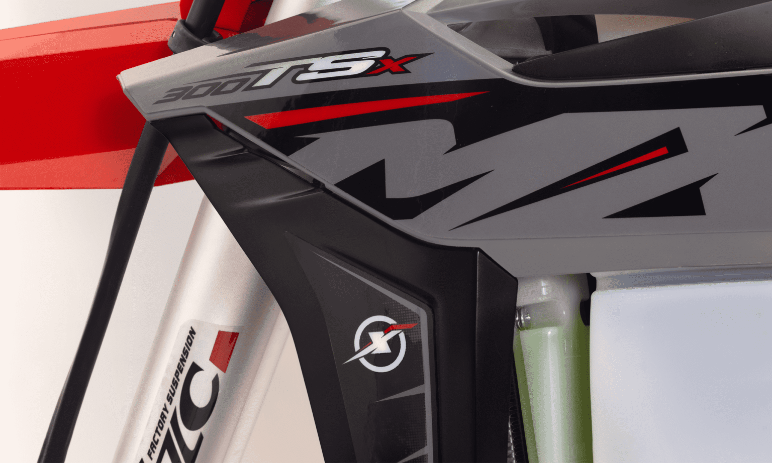 Close no grafismo da MXF 300 TSX na carenagem lateral cinza e vermelha, e a base da suspensão dianteira.