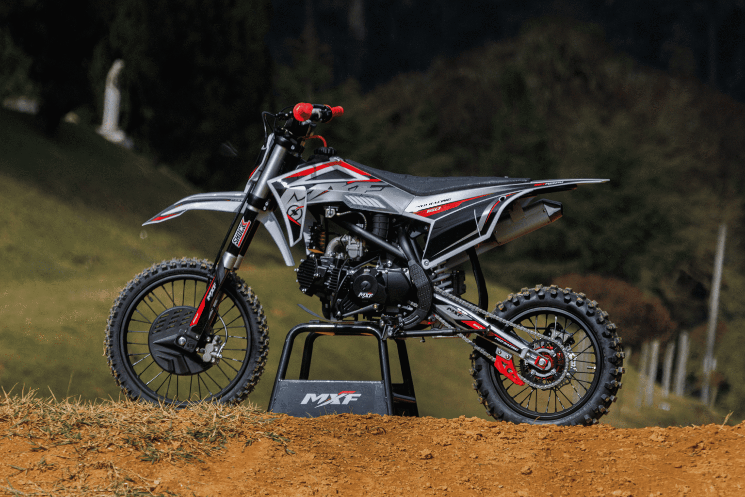 Pit Bike MXF Pro Racing 150 RR vermelha apontada para a esquerda e apoiada em cavalete oficial MXF em cenário off-road - Burt Motos Campinas.